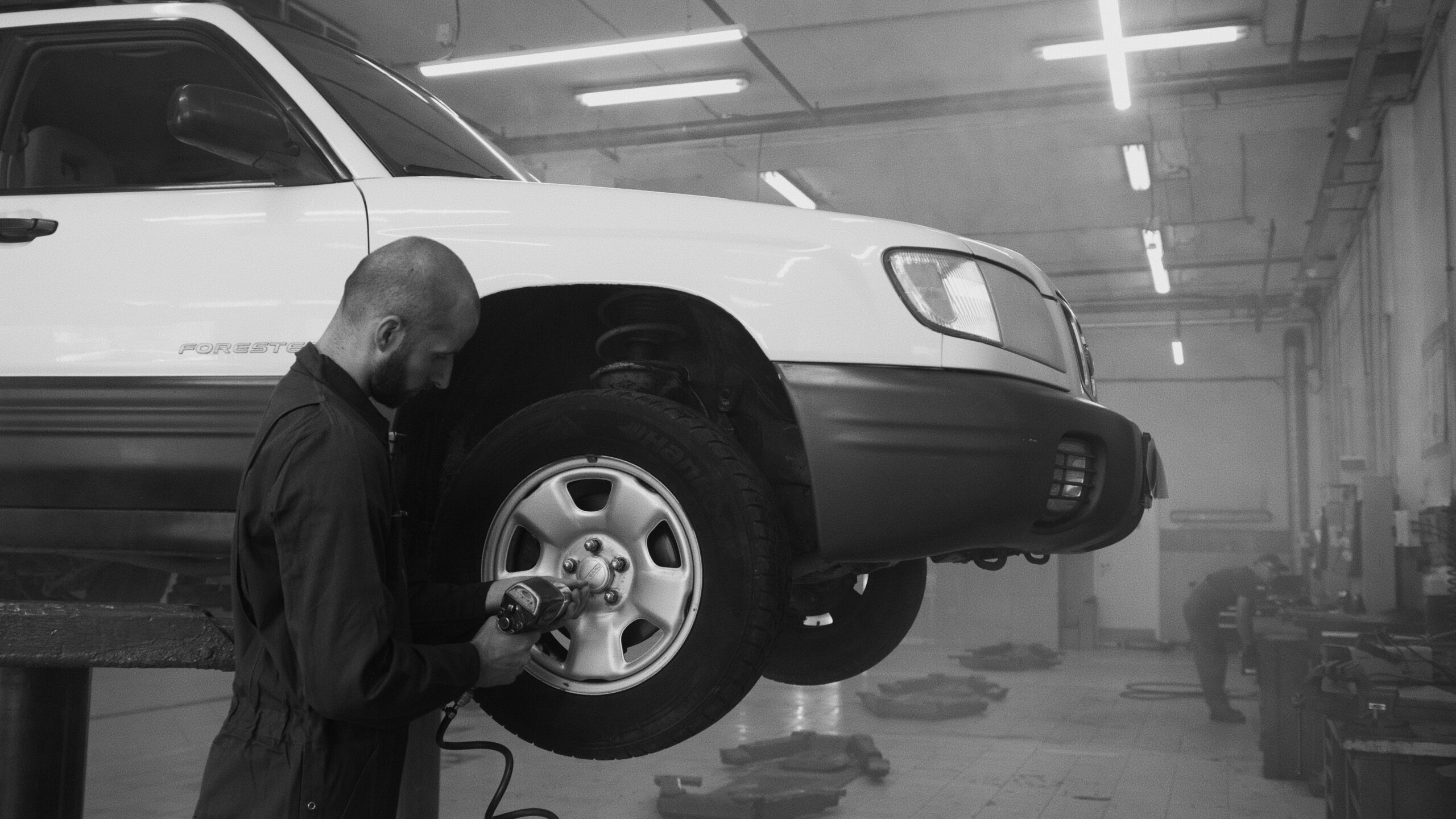 Monochrome image of a mechanic using an impact wrench on a car wheel in a repair shop.